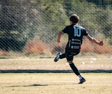 Youth soccer player in motion kicking a ball on a sunny outdoor field.
